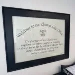 Framed welcome sign for chiropractic clinic mounted on white textured wall