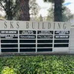Multi-tenant commercial building directory sign listing several businesses including Scorca Chiropractic, with large trees and green foliage below
