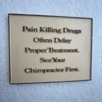 Framed sign with text reading 'Pain Killing Drugs Often Delay Proper Treatment. See Your Chiropractor First.'