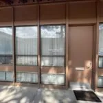 Modern glass and metal entrance door to commercial building with vertical blinds visible through windows and concrete entryway