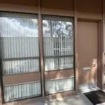 Brown glass entrance door with vertical blinds and a doormat in front of a building entryway